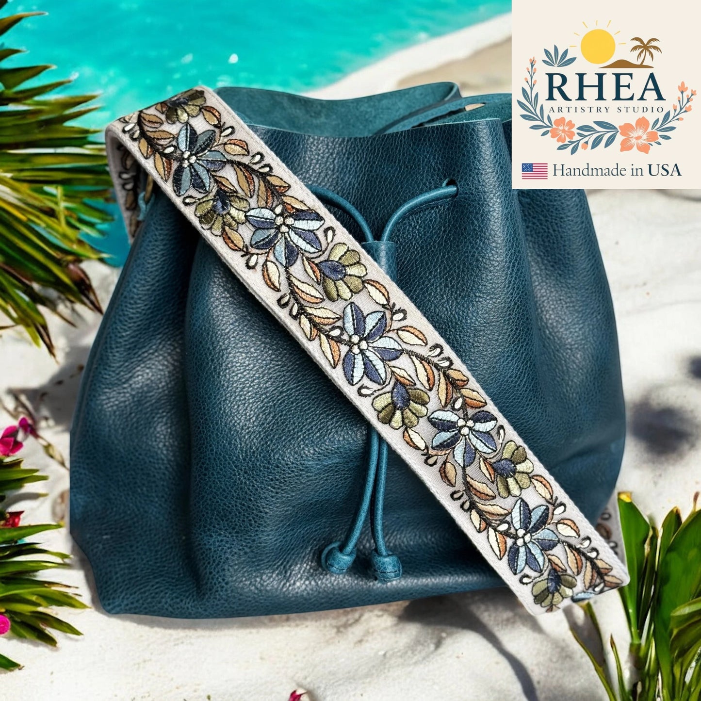 Blue leather bag with a floral purse strap on a natural background, featuring the RHEA Artistry Studio logo.