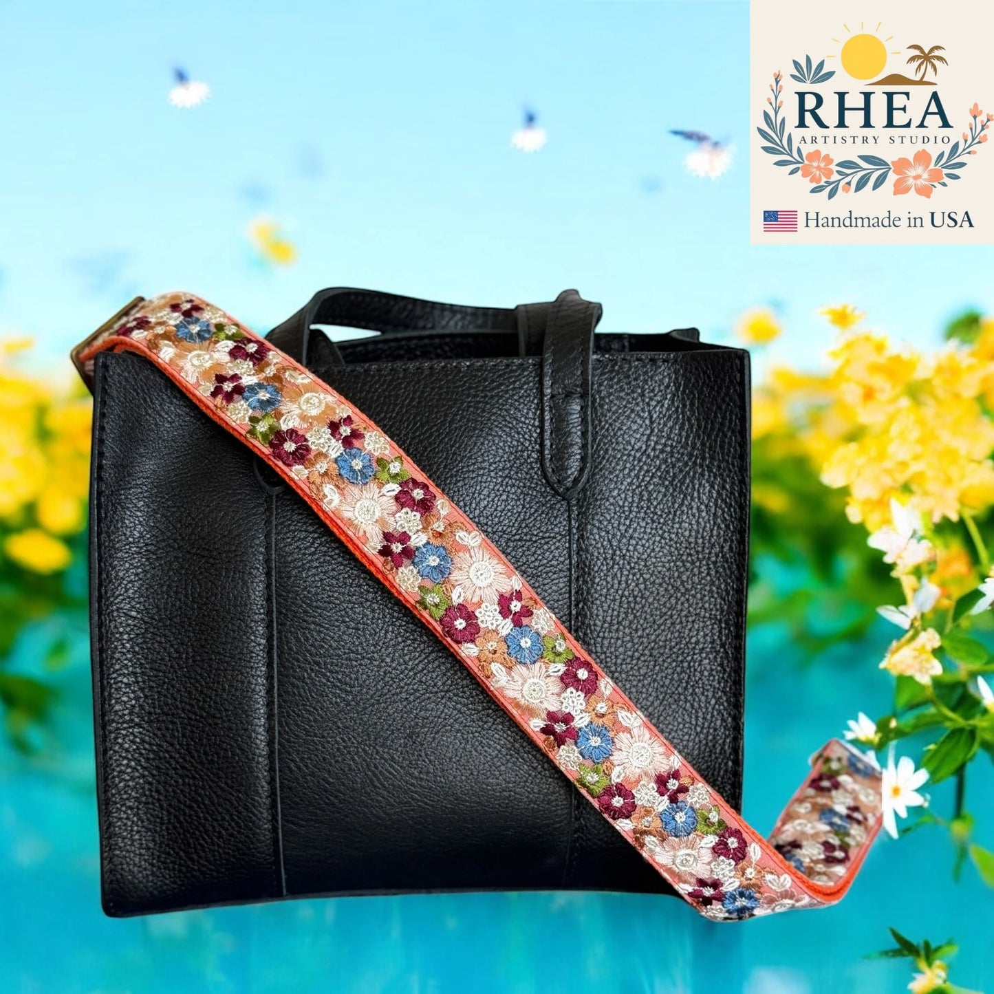 Black handbag with a floral purse strap against a floral background, featuring the RHEA brand.