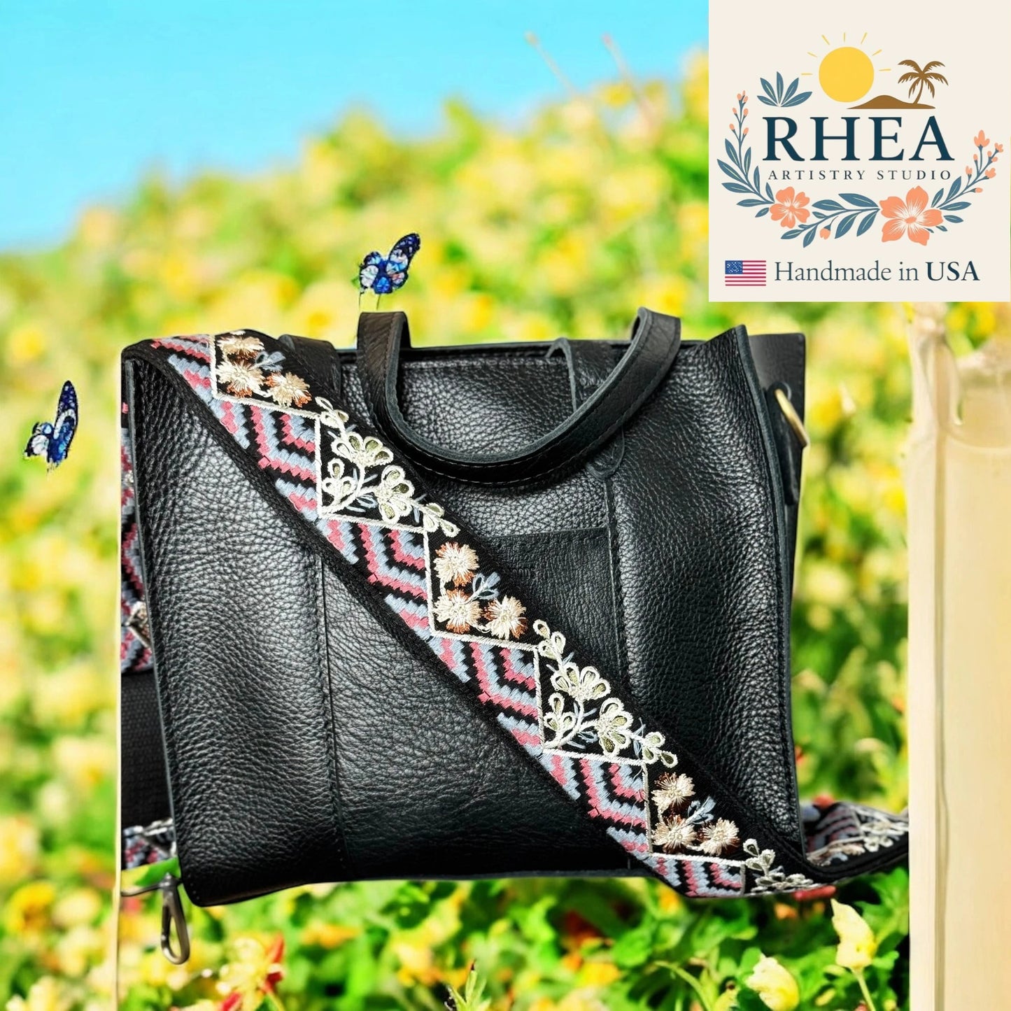 Black handbag with embroidered strap against a blurred natural background, featuring the RHEA Artistry Studio logo.