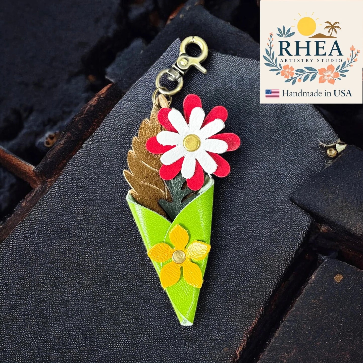 Floral-themed leather boquest charm with 'RHEA' branding on a dark textured background