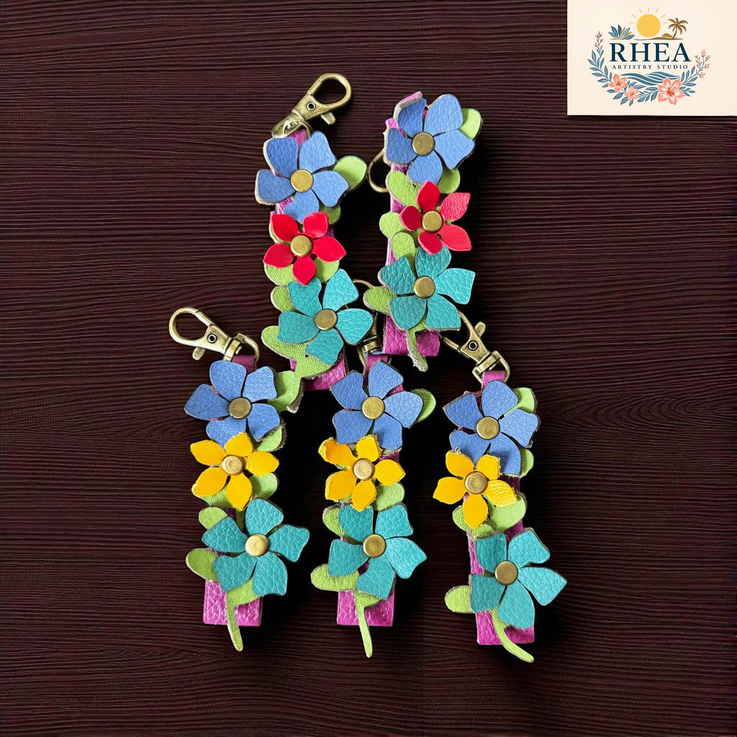 Colorful flower-shaped keychains on a brown background with RHEA logo.