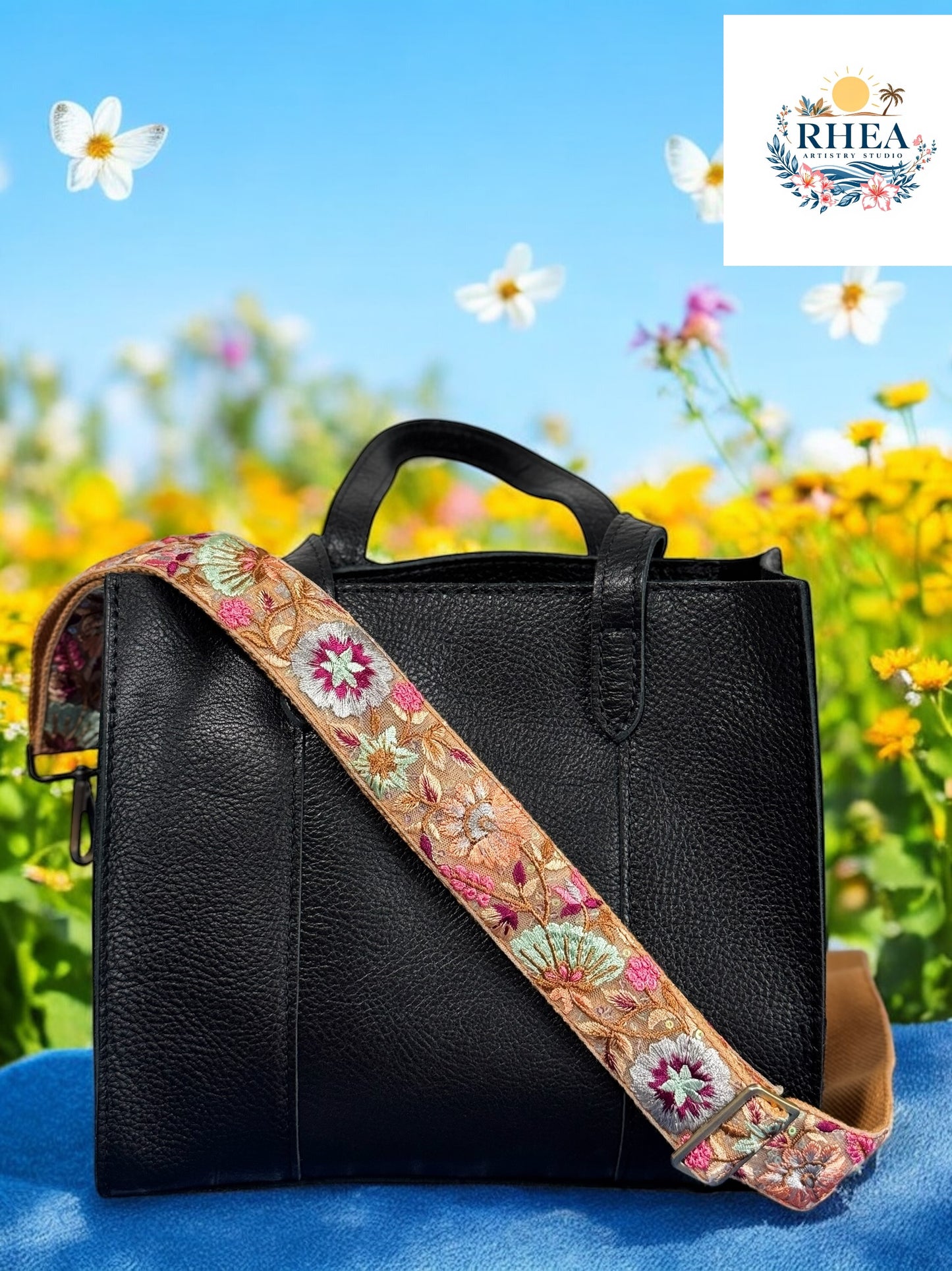 A black handbag with a floral embroidered strap placed against an outdoor backdrop with yellow flowers.