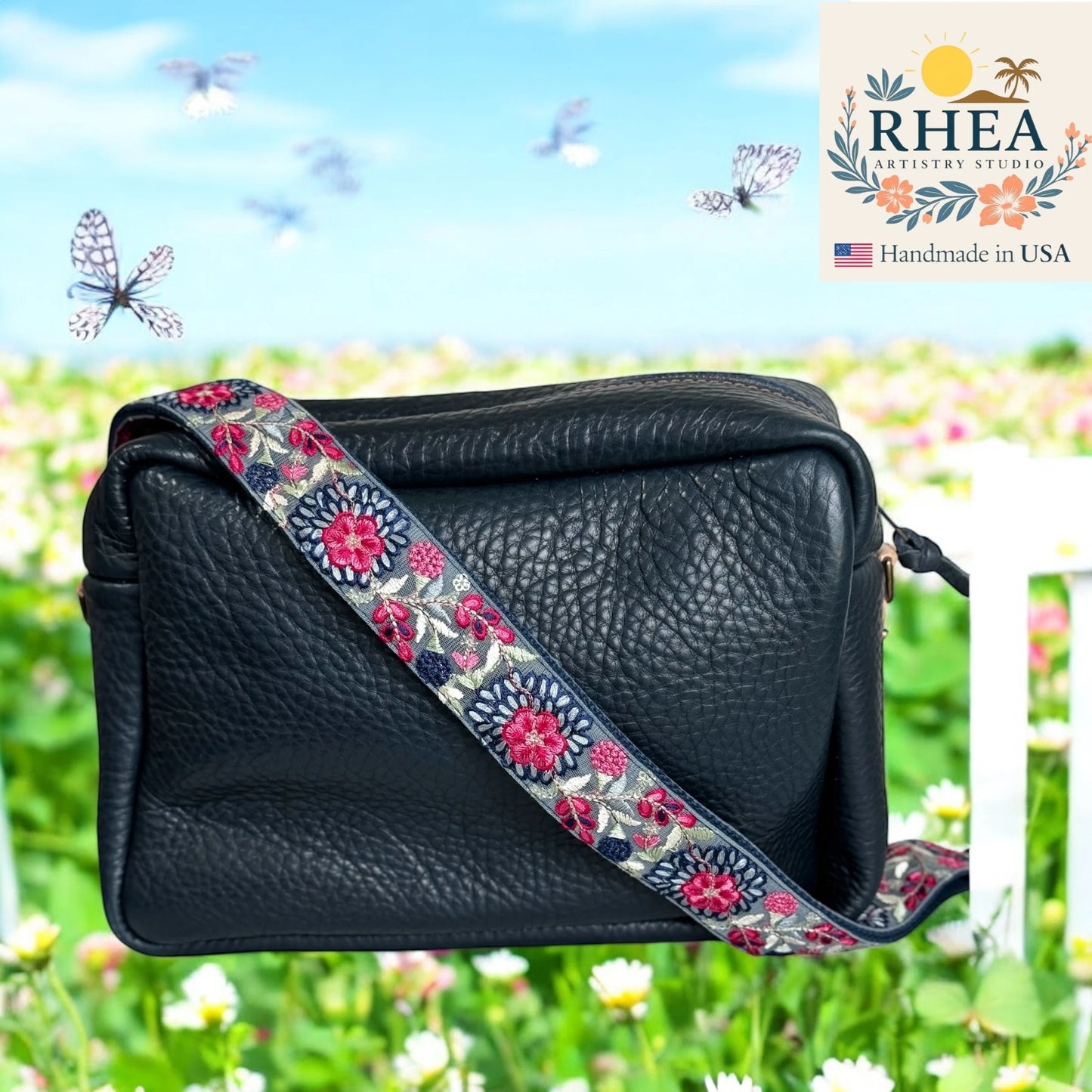 Black leather handbag with a floral purse strap against a natural background, featuring the RHEEA brand.