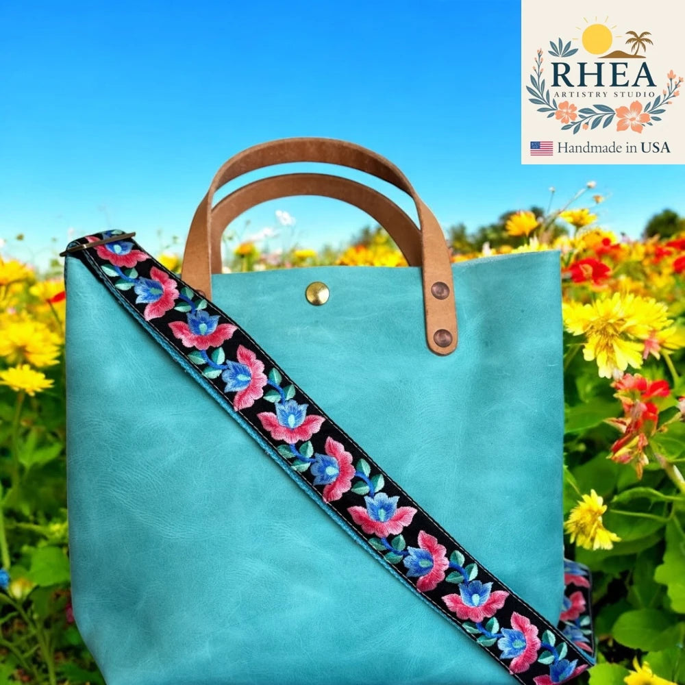 Turquoise tote bag with floral purse strap in a field of flowers, featuring the RHEA brand.