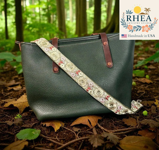 Green handbag with floral strap on a forest floor, RHEEA brand visible