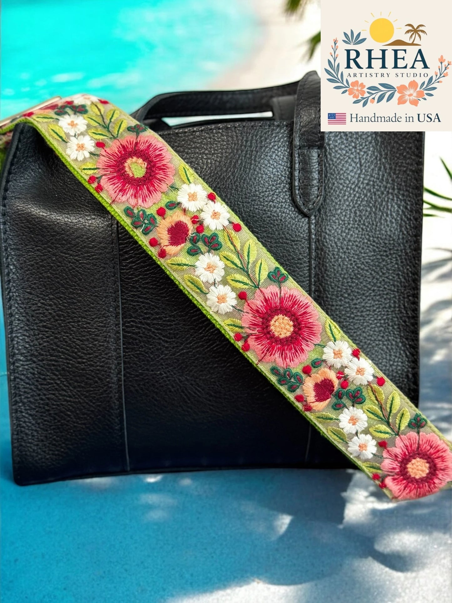 Black handbag with a floral purse strap on a blue surface, featuring the RHEA brand.