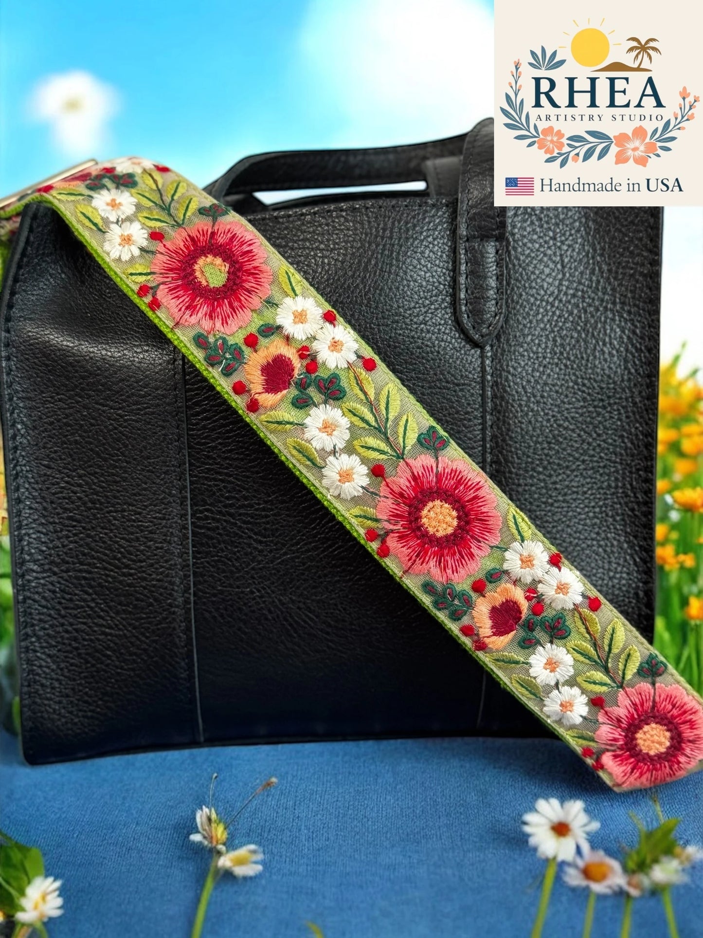 Black handbag with a floral purse strap against a blue background, featuring the RHEA Artistry Studio logo.