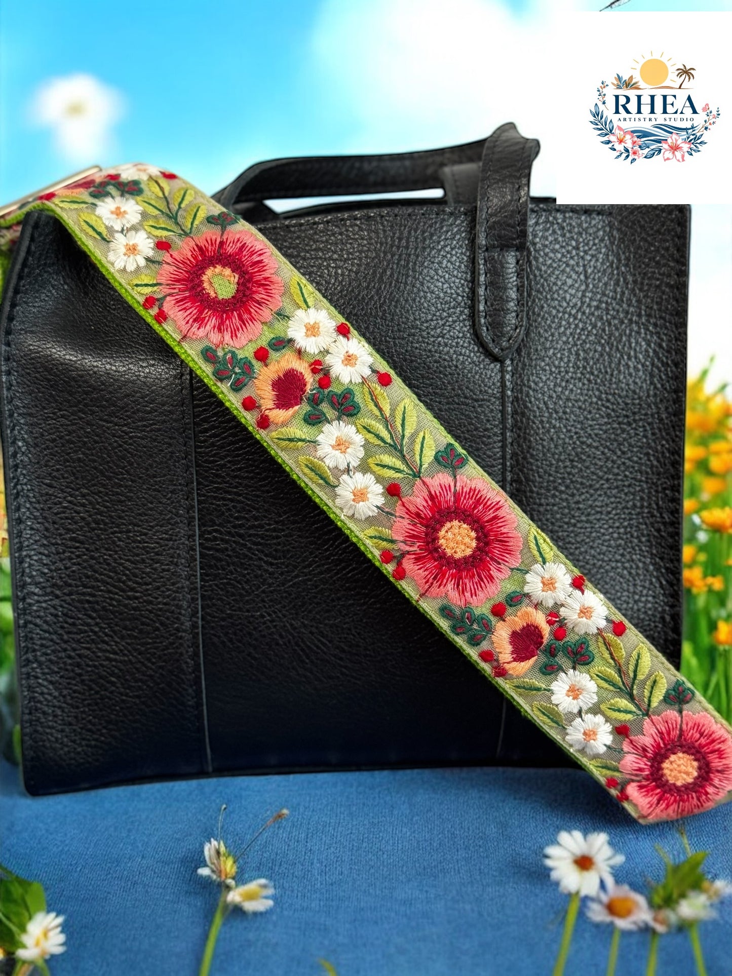 Olive green floral crossbody strap with crimson daisies and ivory blossoms attached to a structured black leather handbag.