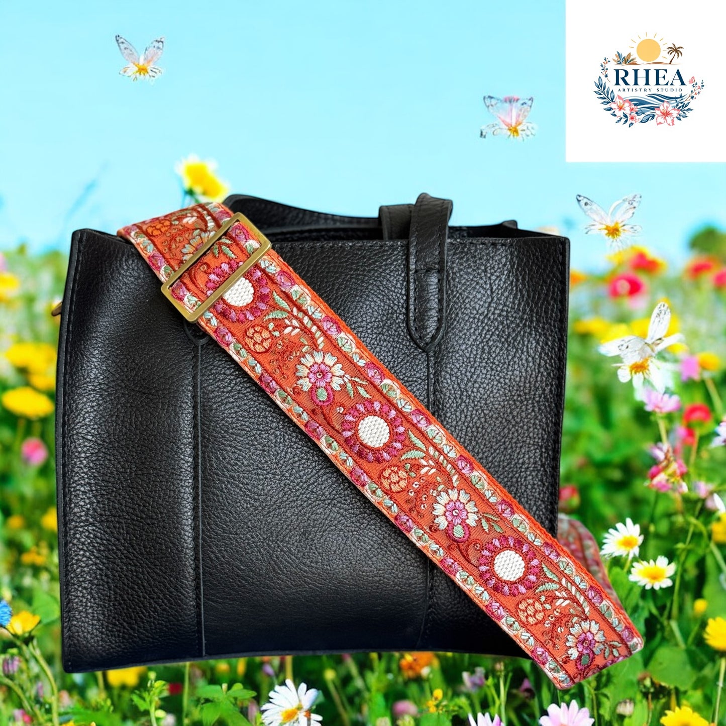 Black leather bag with an embroidered strap in marigold-orange featuring pink, white, and green floral and geometric designs, set against a meadow of daisies and butterflies.