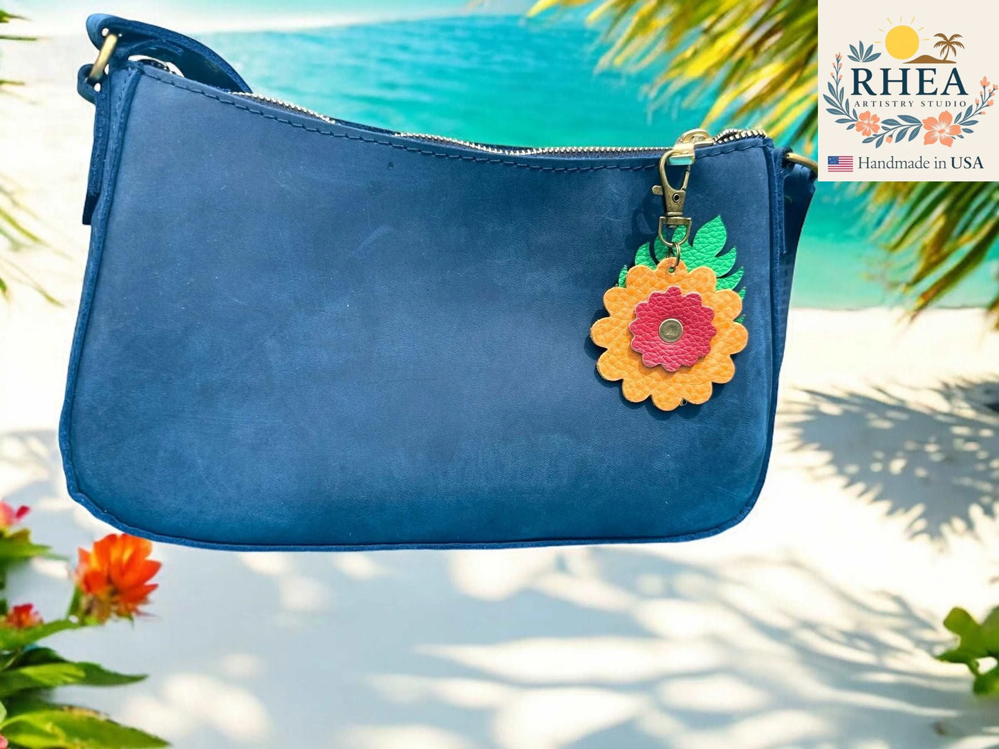 Blue handbag with a bag charm on a beach background, featuring the RHEA brand.