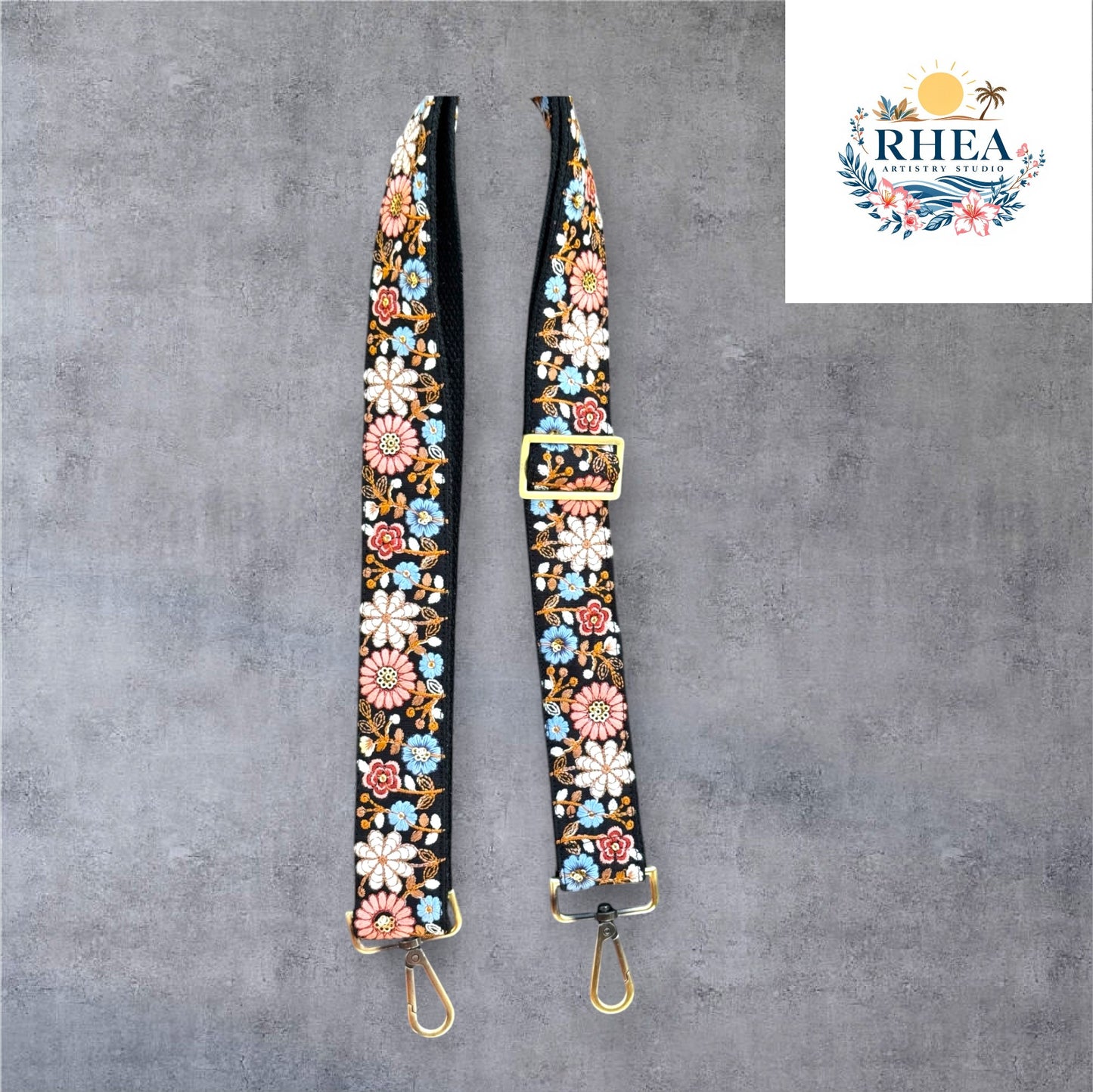 An adjustable strap with daisy flowers embroidery attached to a black bag, with a field and sunset in the background.