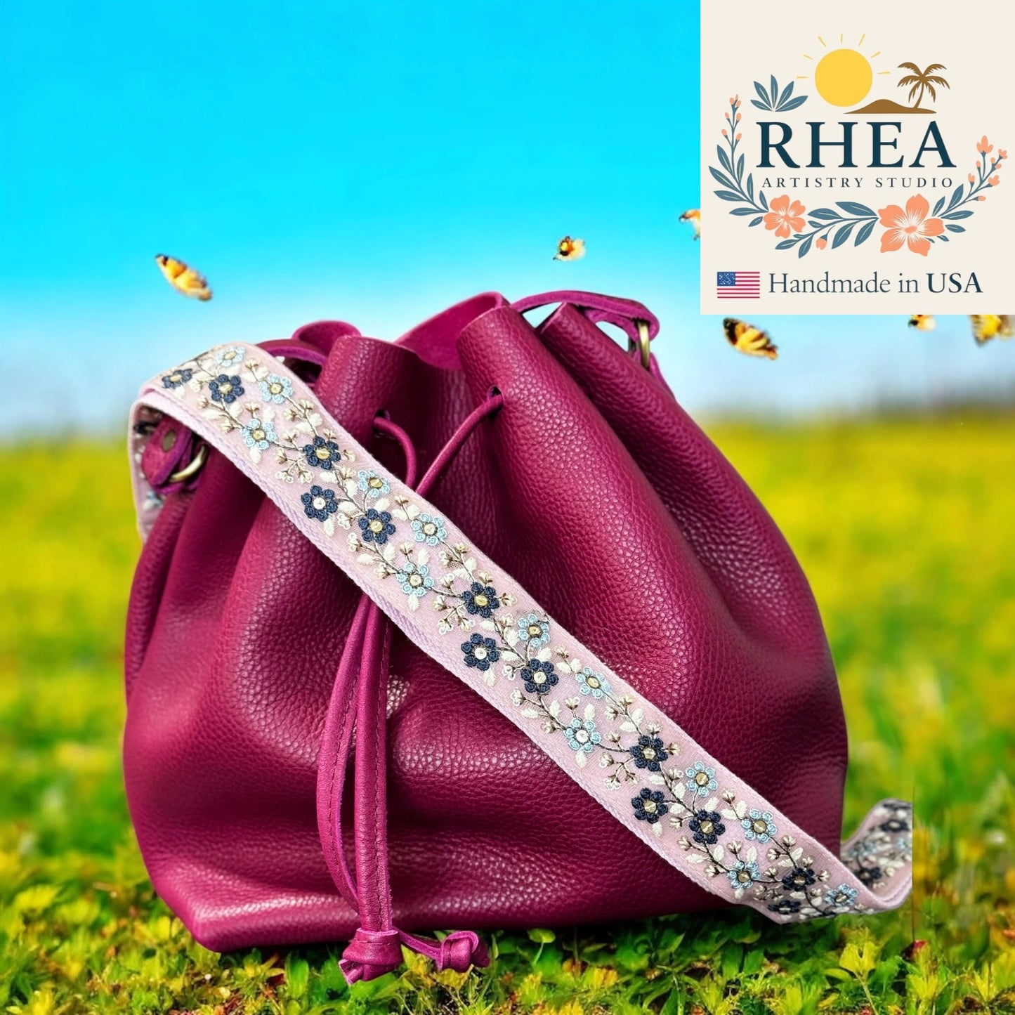 Purple leather bag with floral strap on grass, RHEA Artistry Studio logo visible