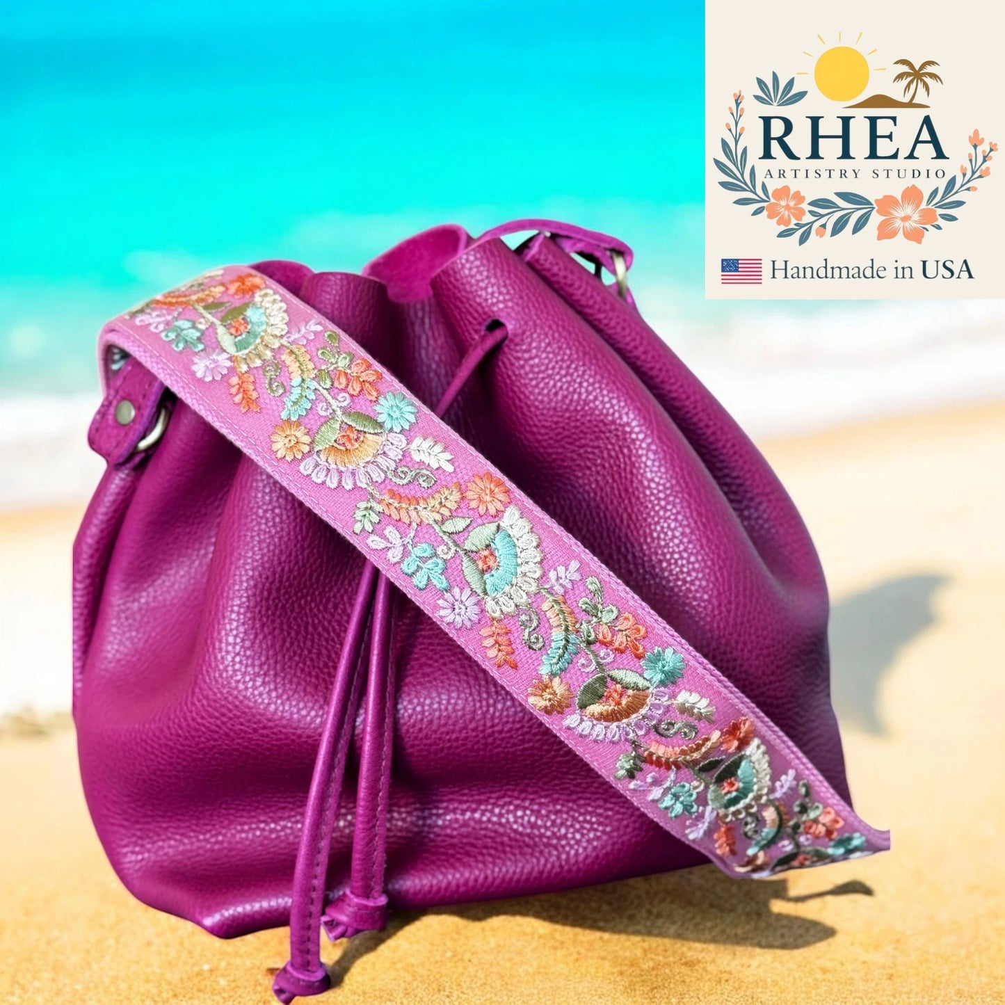 Pink drawstring bag with floral strap on a beach, featuring RHEA Artistry Studio logo.