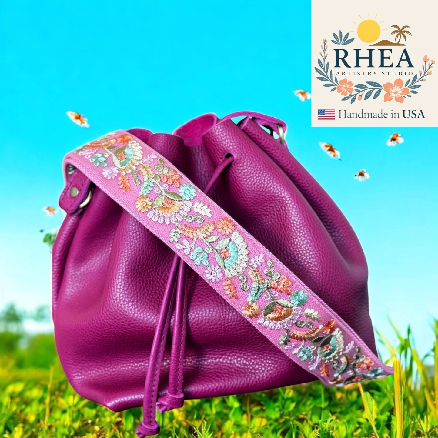 Purple drawstring bag with floral strap on grass with blue sky, RHEA brand visible