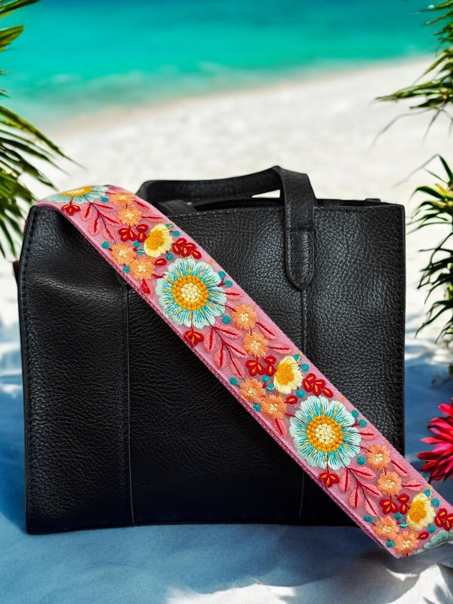 Pink floral embroidered purse strap with sky blue and maroon blooms styled on a black leather bag at beach