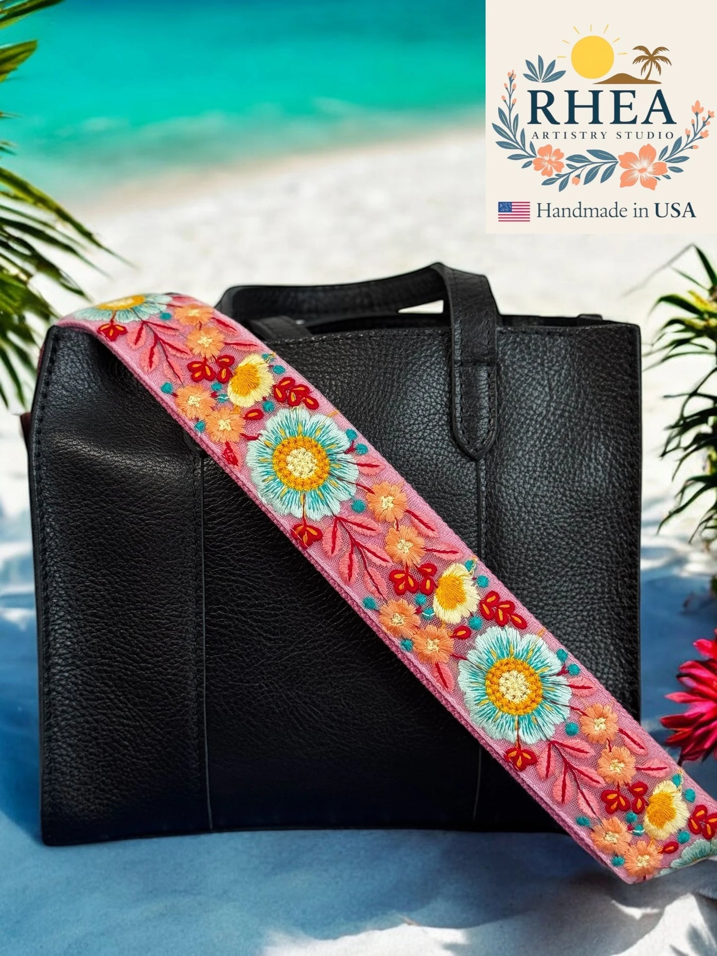 Black bag with a colorful floral purse strap on a beach background, featuring the RHEA brand.