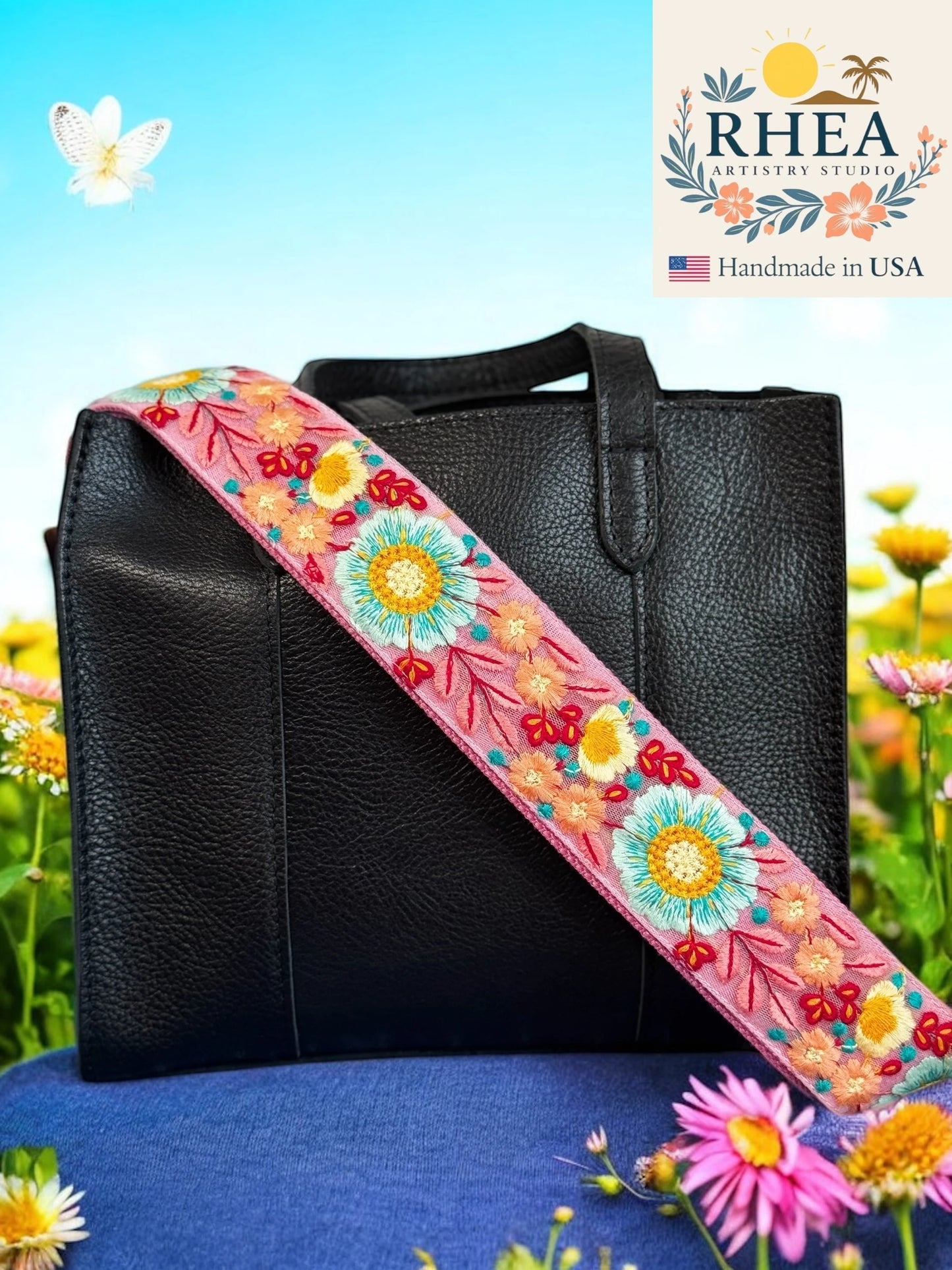 Black leather bag with a colorful floral purse strap against a natural background, featuring the RHEA brand.