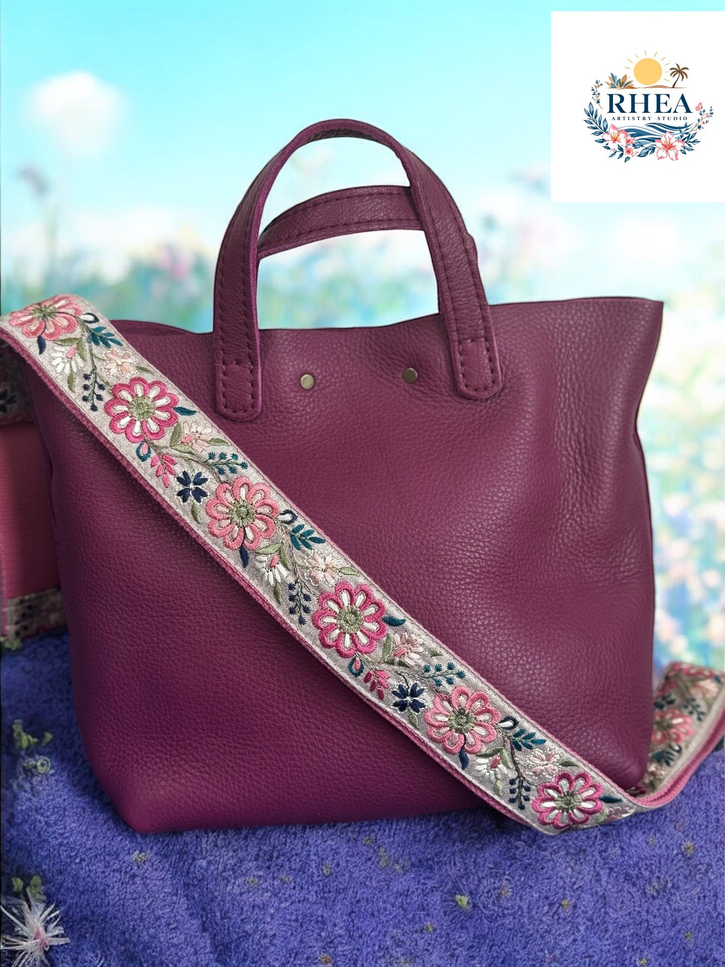 Magenta handbag with vibrant pink and white floral strap in pinwheel embroidery set against a garden backdrop.