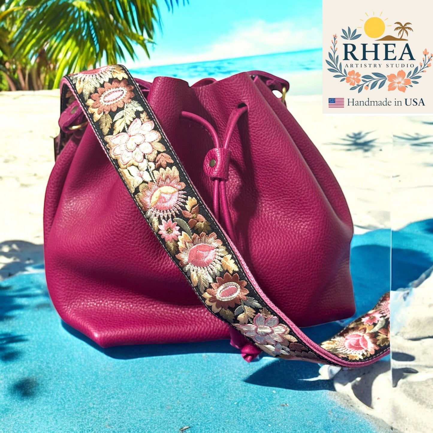 Pink handbag with floral purse strap on a beach, featuring RHEA branding.