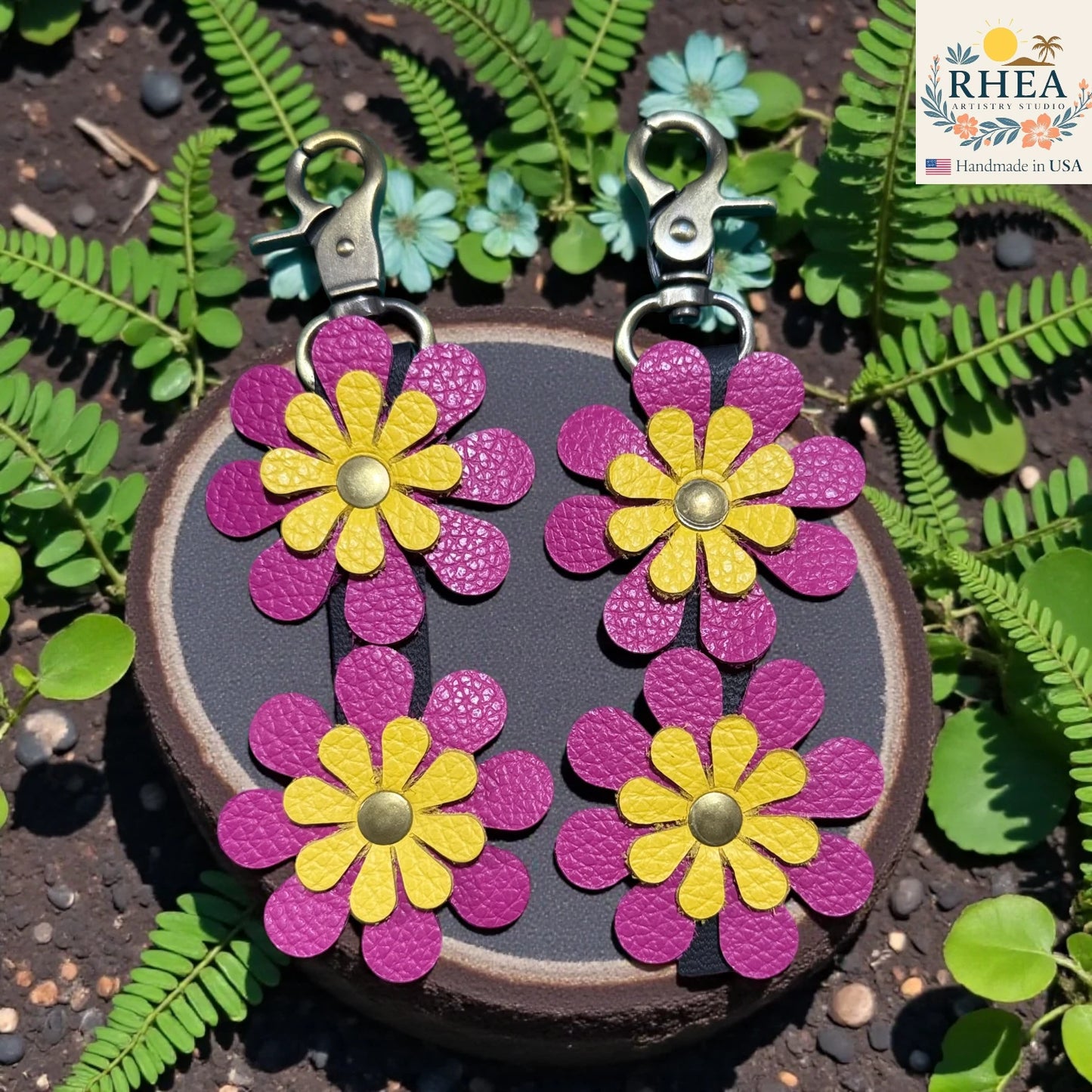 Flower-shaped keychains on a round wooden block with green leaves in the background, featuring the RHEEA brand.
