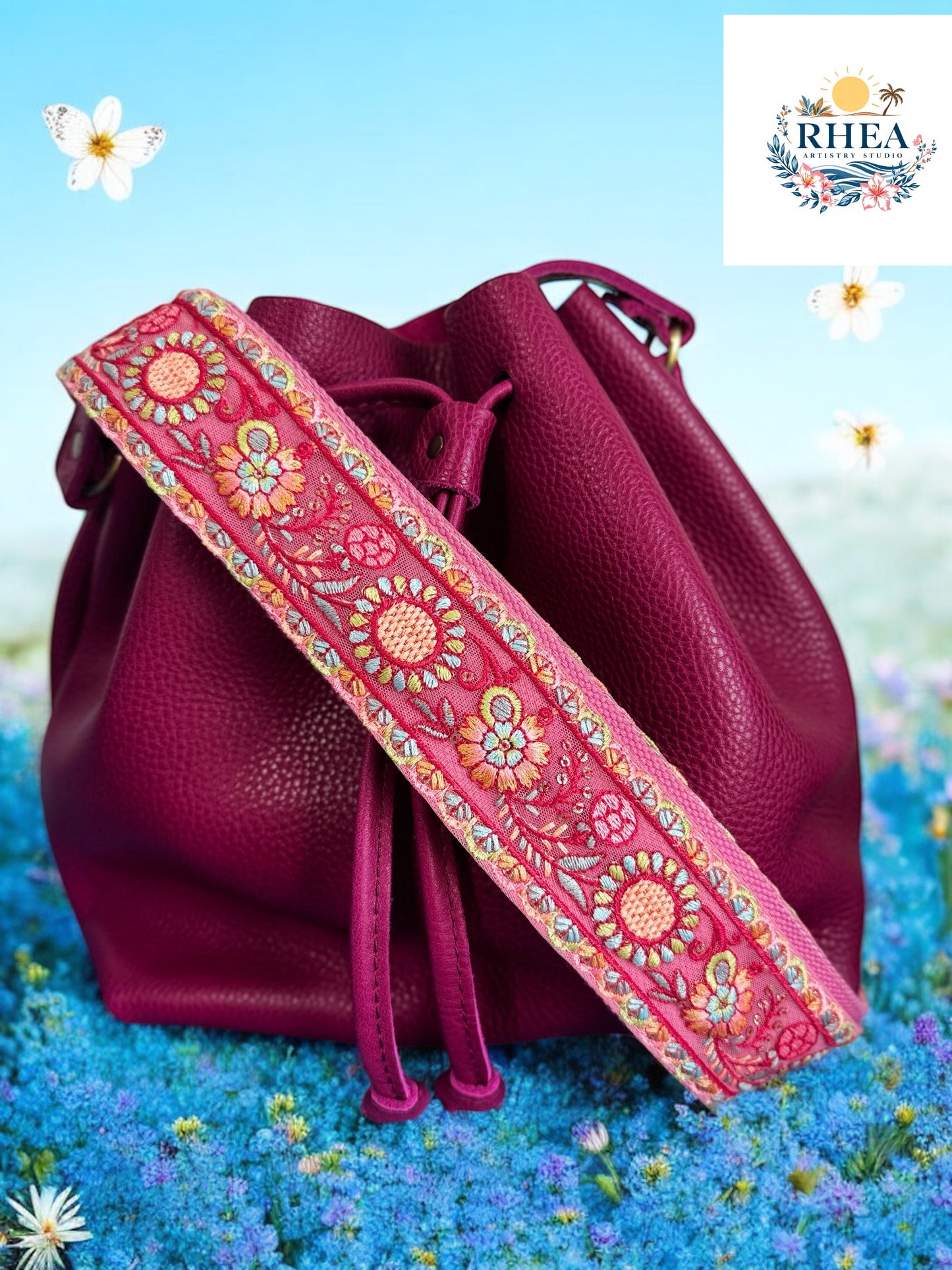 Handcrafted purse strap in soft pink with embroidered zinnias and teal accents, shown on a magenta leather bag.