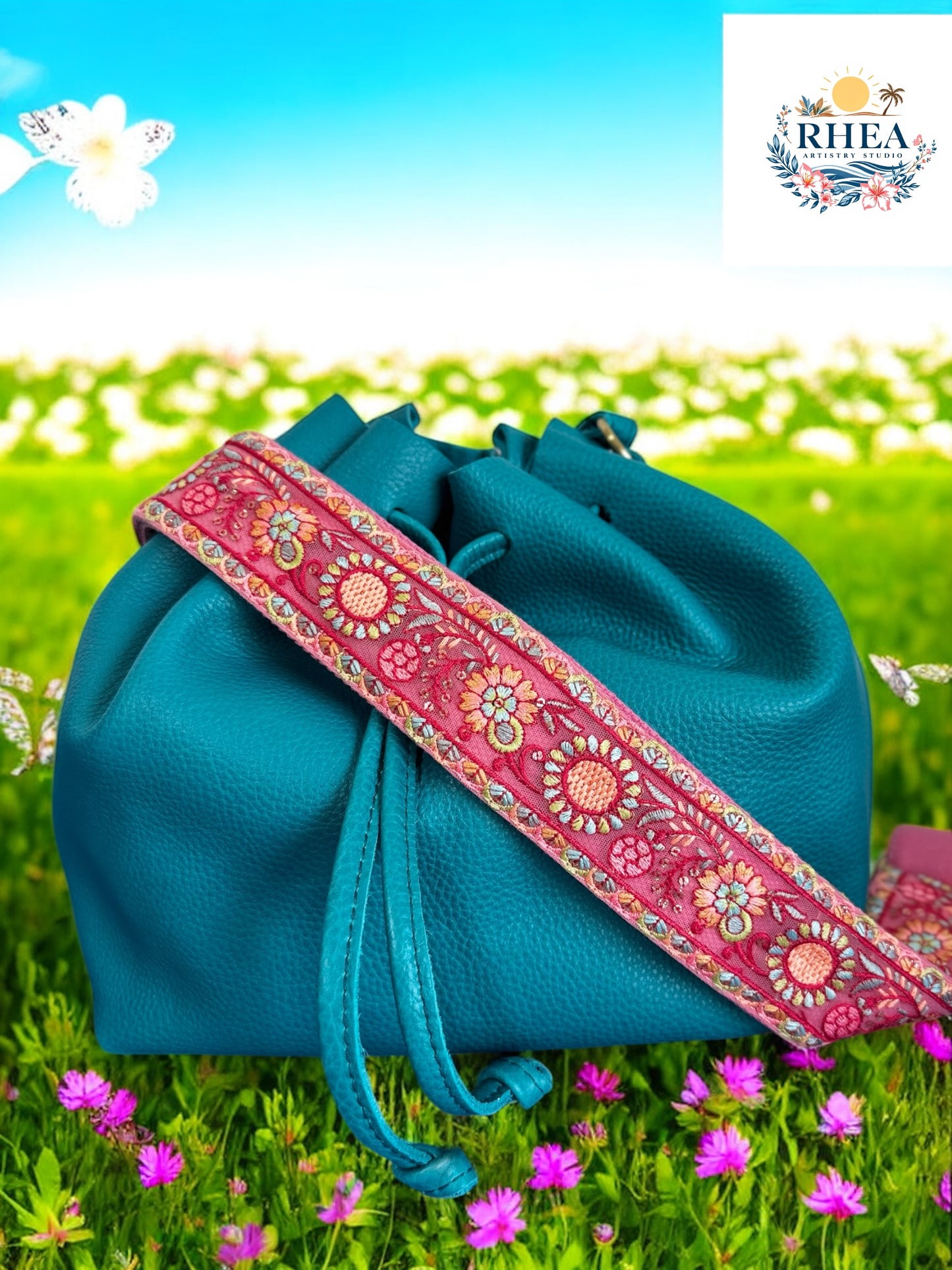 Handcrafted purse strap in soft pink with embroidered zinnias and teal accents, shown on a turquoise leather bag.