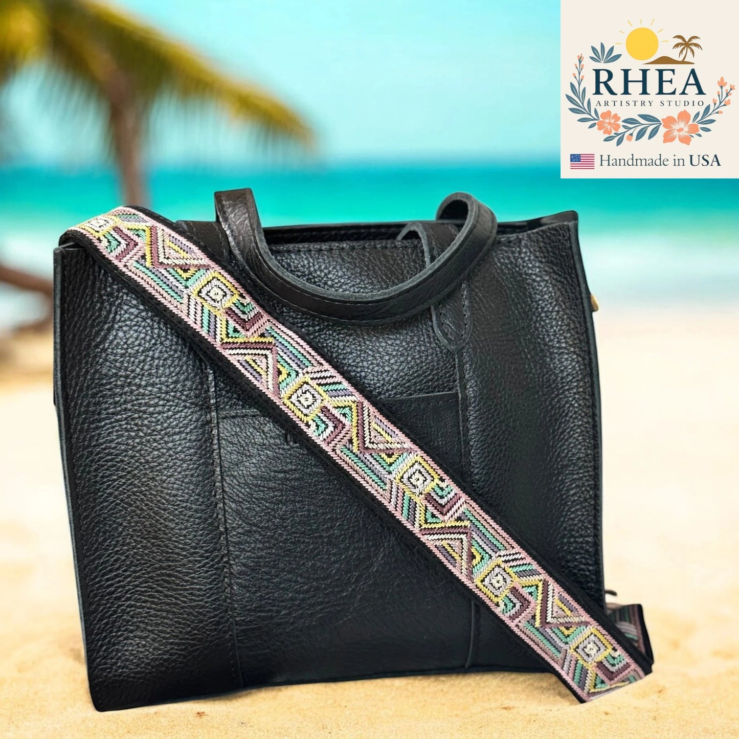 Black leather handbag with a colorful strap on a beach background, featuring the RHEA brand.