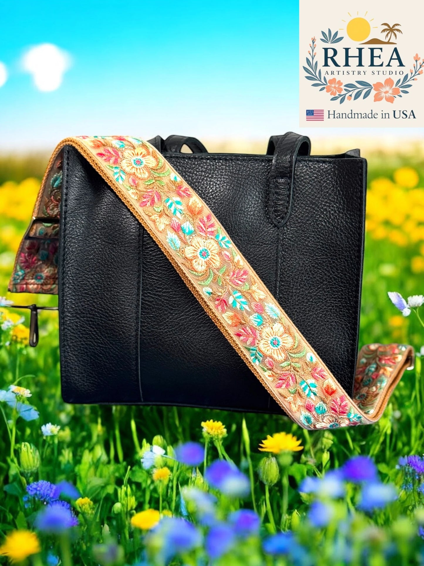 Black handbag with a colorful floral purse strap in a field of flowers, featuring RHEA Artistry Studio branding.