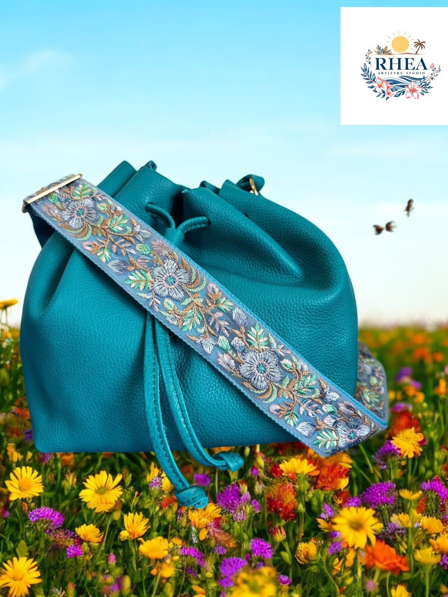 A black purse with a plum blue floral embroidered purse strap set against a field of colorful flowers.