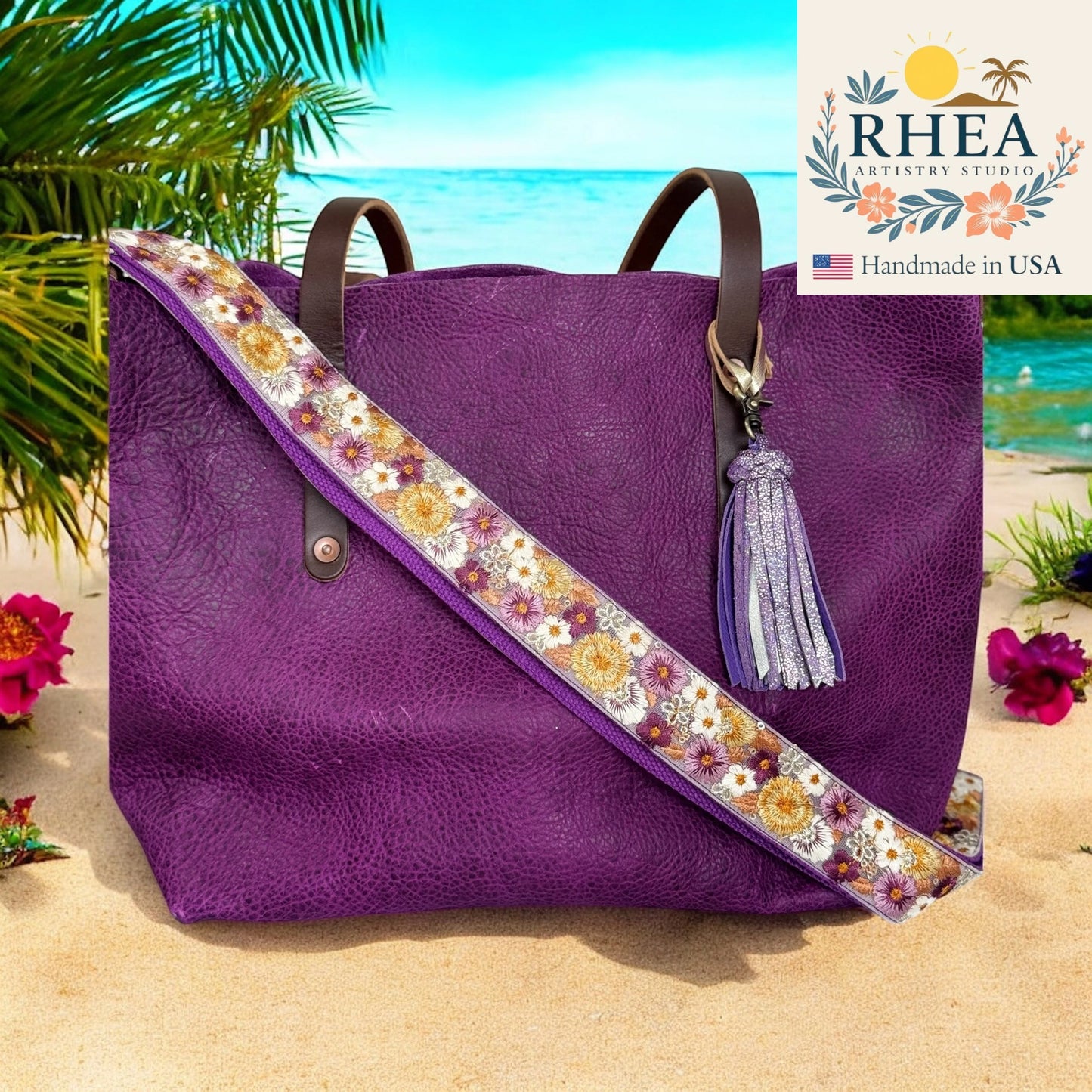 Purple tote bag with floral purse strap and tassel on a beach, featuring the RHEA Artistry Studio logo.