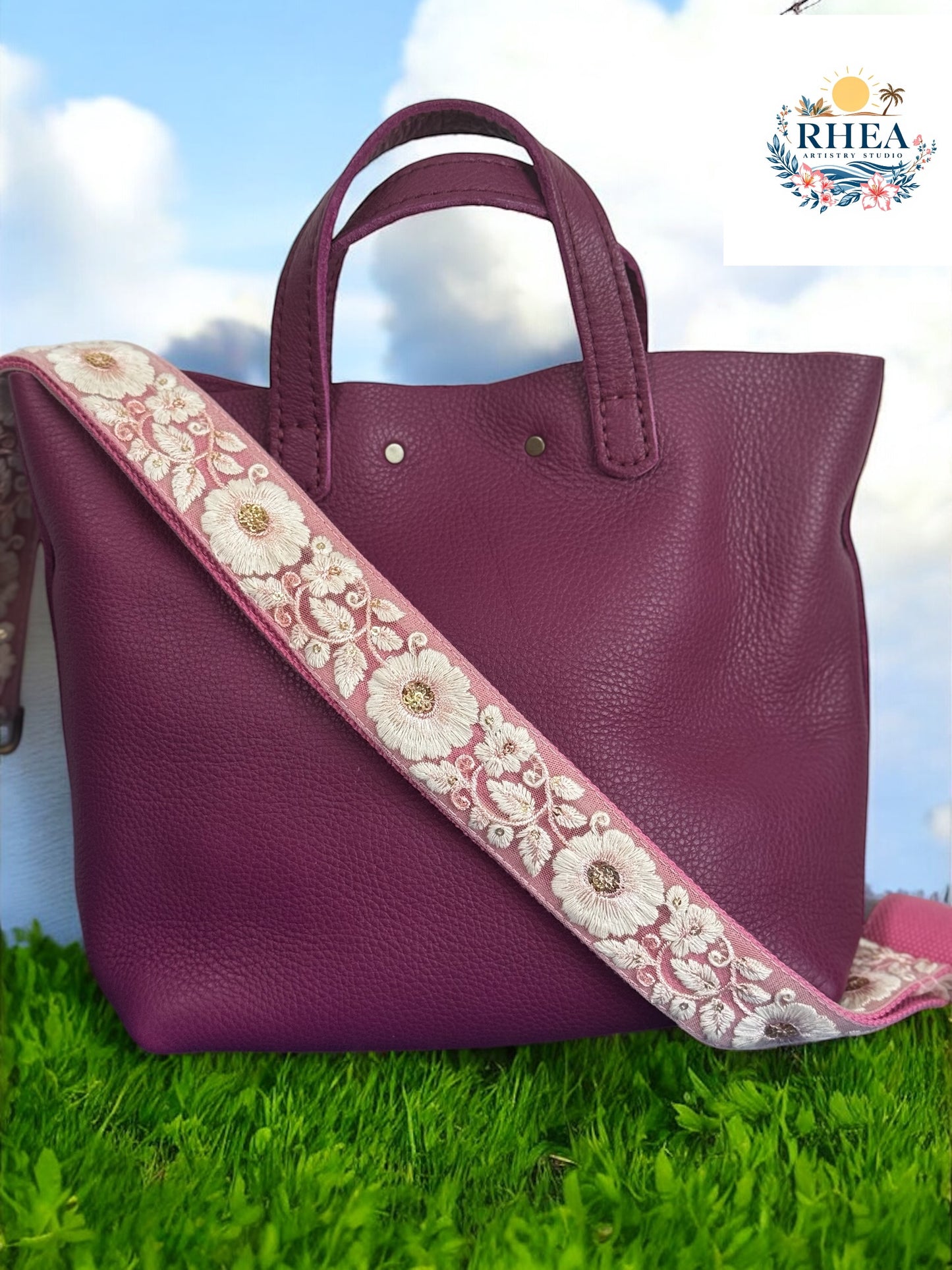 A black purse with a beige and green floral embroidered strap placed on a blue surface with a floral background.