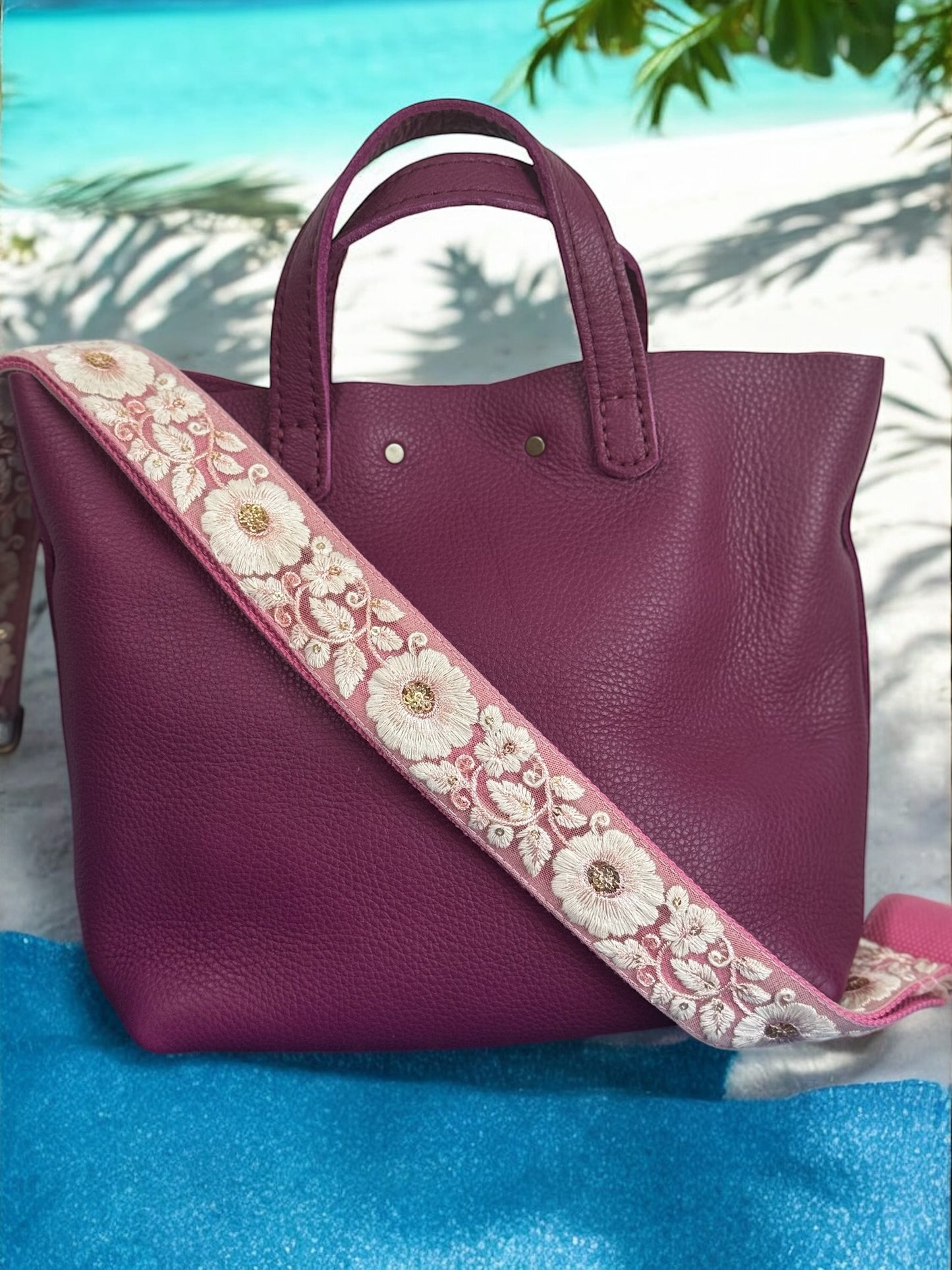 A black purse with a beige and green floral embroidered strap placed on a blue surface with a floral background.