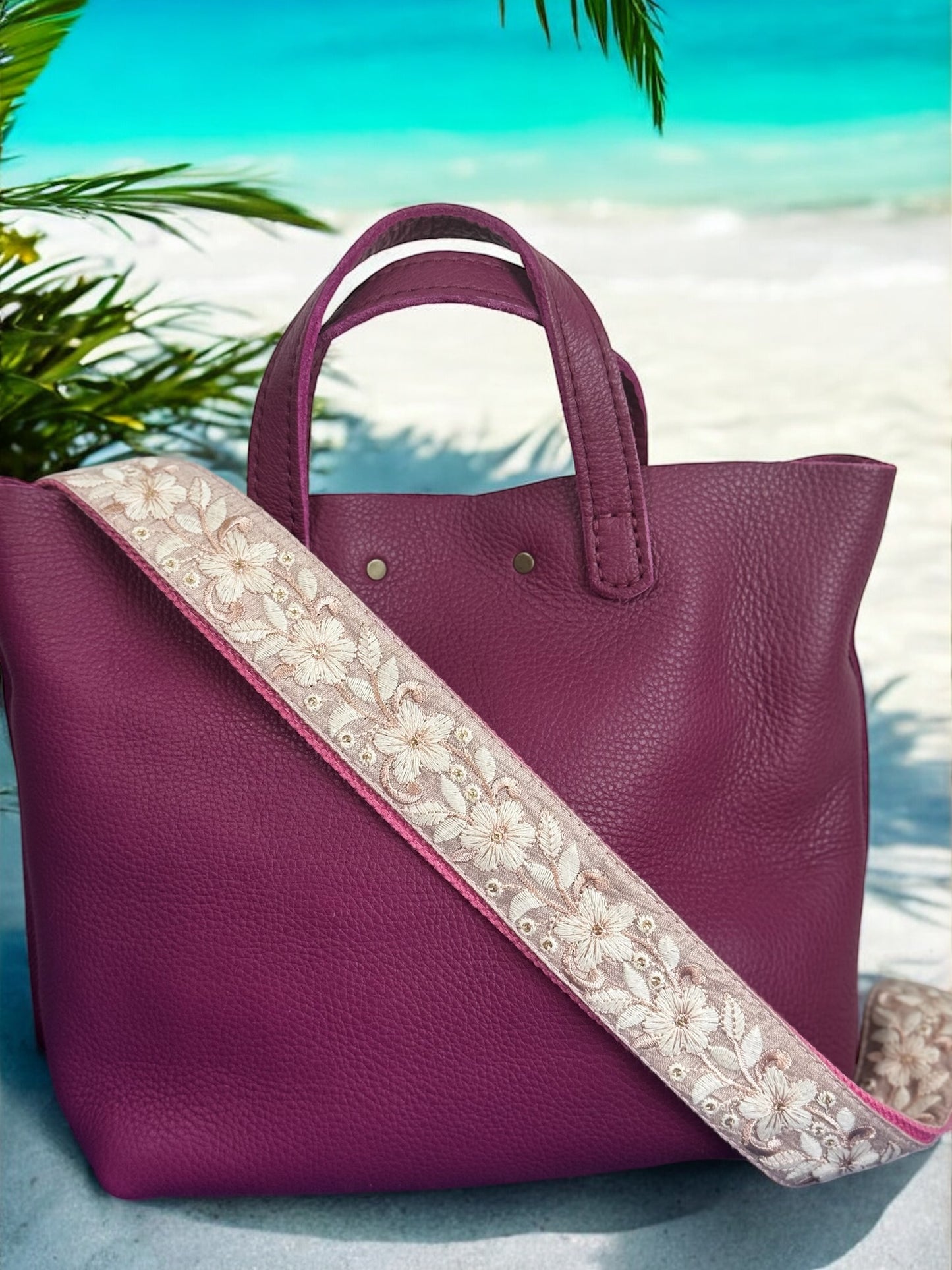 A black purse with a floral patterned strap, displayed against a blue background with floral motifs.