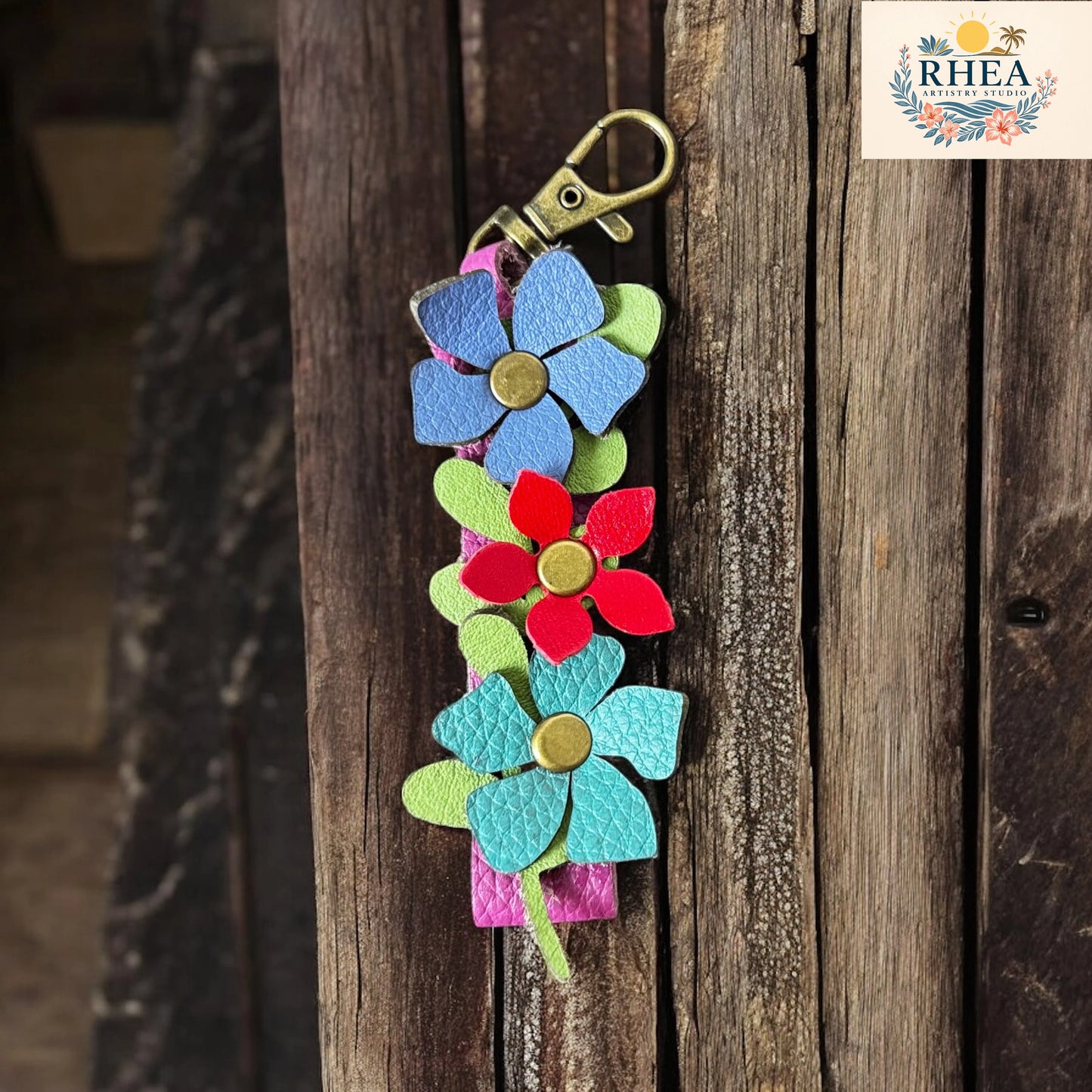 Colorful flower-shaped keychain on a wooden surface with RHEEA branding.