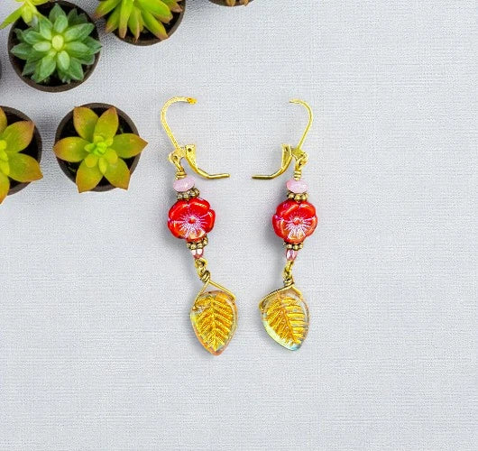 Pair of earrings with red floral and gold leaf designs on a light gray background.