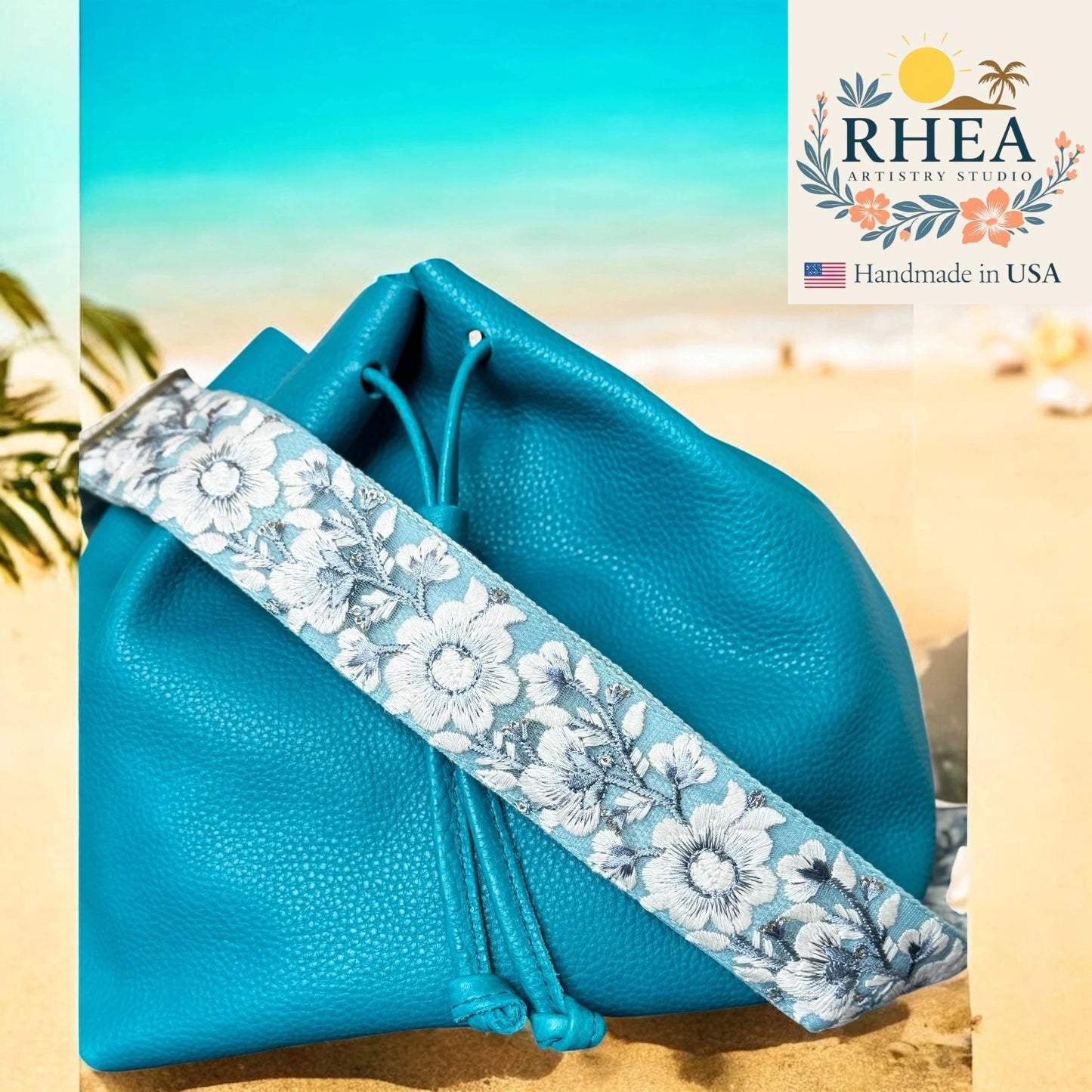 Blue pouch with floral strap on a beach background, featuring RHEA Artisan Studio logo.