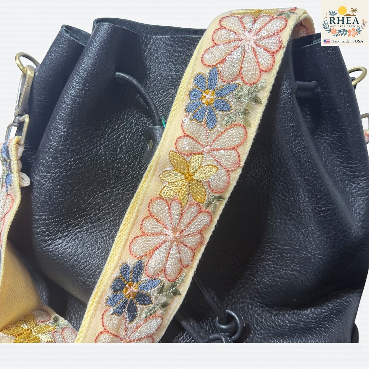 Black leather bag with a floral embroidered purse strap on a white background
