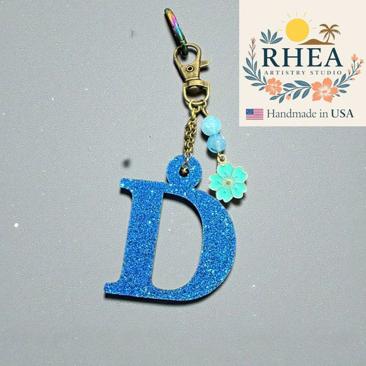 Rhea Artistry Studio blue glitter letter D charm with blue beads and a teal flower charm, attached to a keychain clasp.