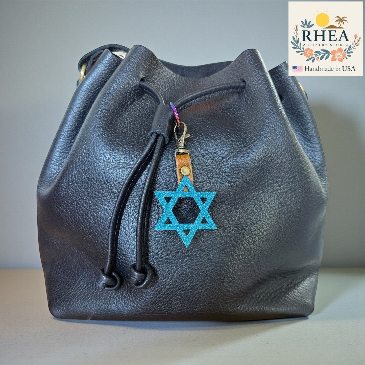 Rhea Artistry Studio blue glitter Star of David charm attached to a black leather drawstring bag.