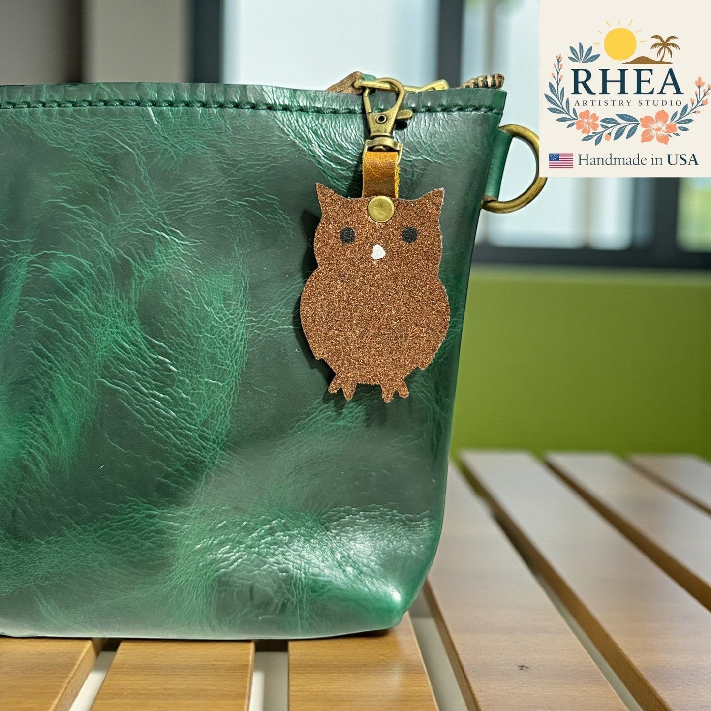 Rhea Artistry Studio brown glitter owl charm with white eyes and beak, attached to a green leather bag.