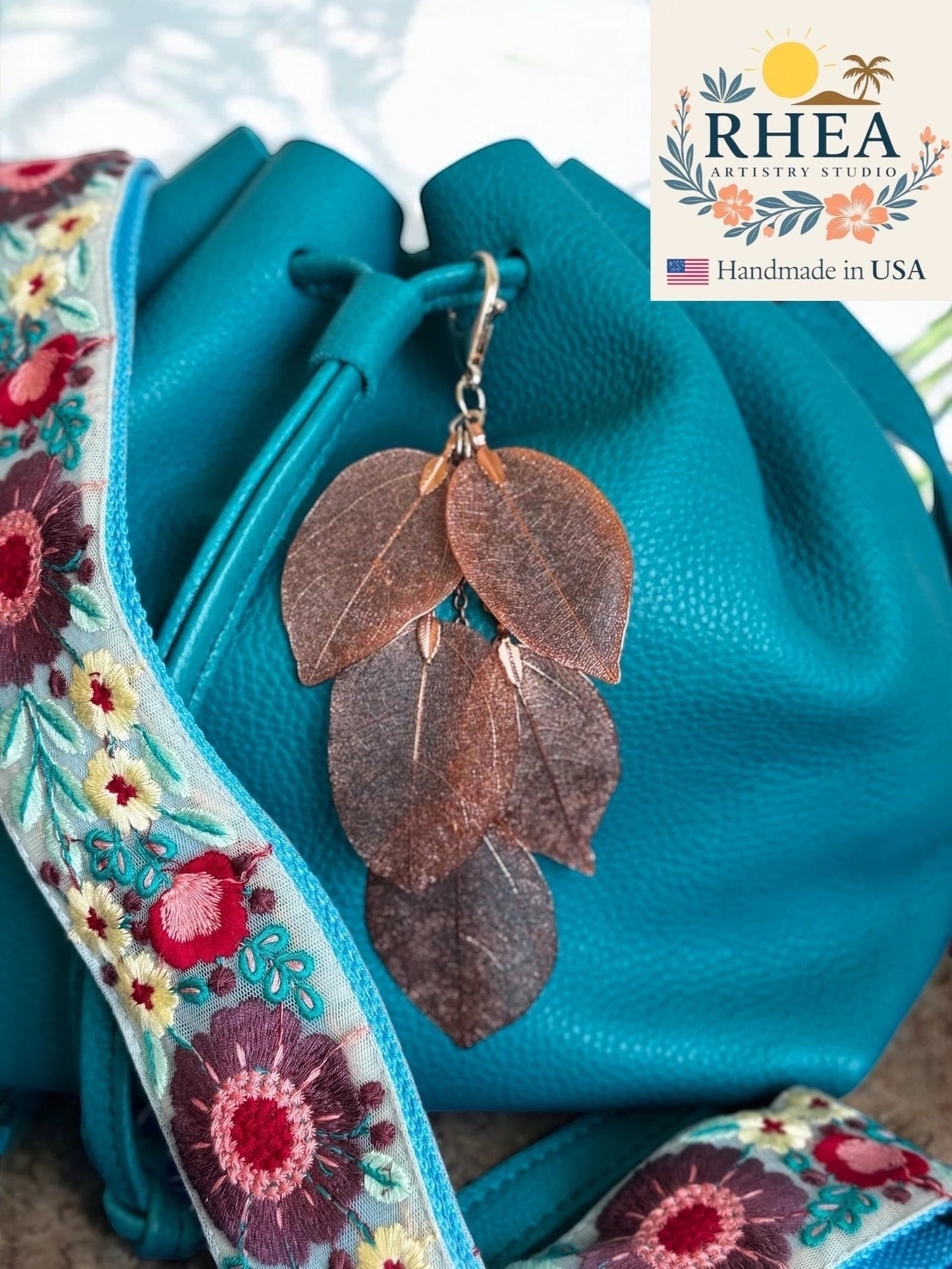 Rhea Artistry Studio copper metallic leaf bag charm with delicate veining, attached to a teal leather bucket bag.