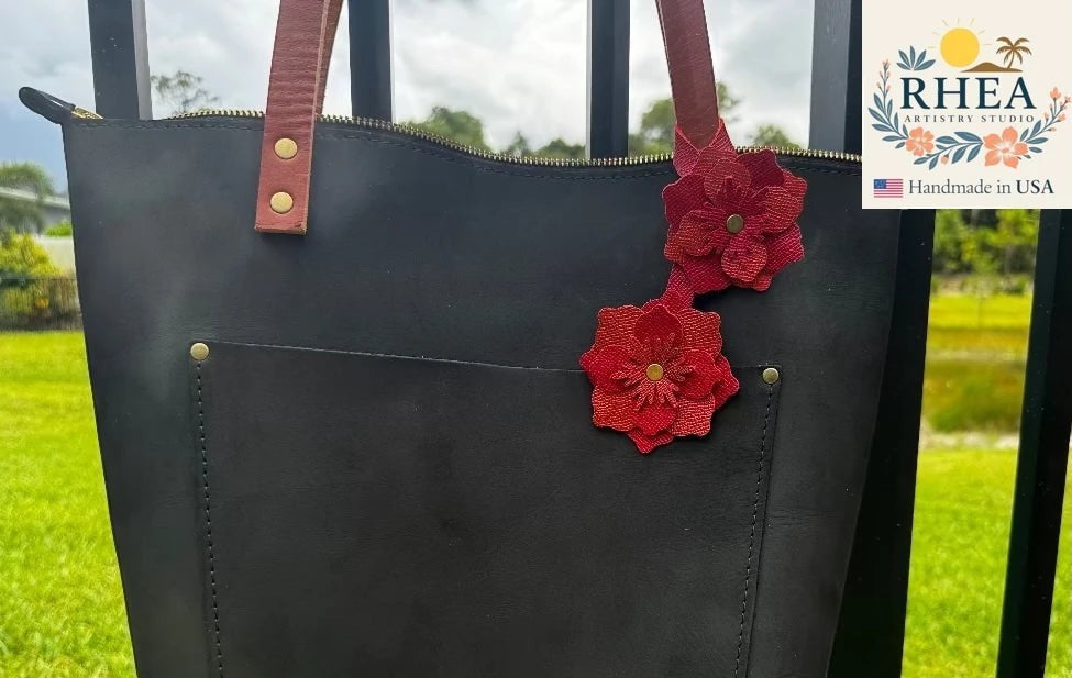 Rhea Artistry Studio double leather flower charm in red and brick red, attached to a black leather tote bag.