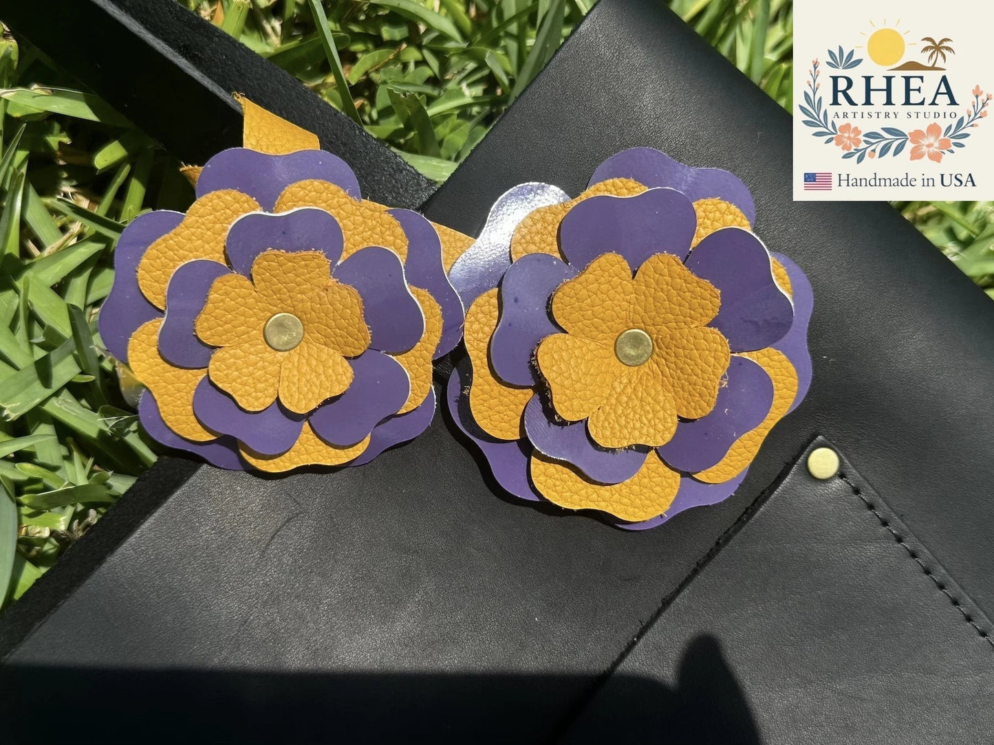 Rhea Artistry Studio eggplant and yellow double leather flower accessory with brass rivets on a black bag.