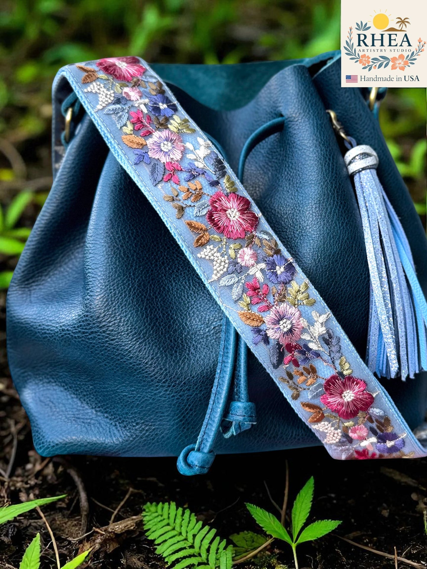 Rhea Artistry Studio light blue crossbody strap with vibrant floral embroidery, 2-inch width, adjustable length, and brushed brass hardware.
