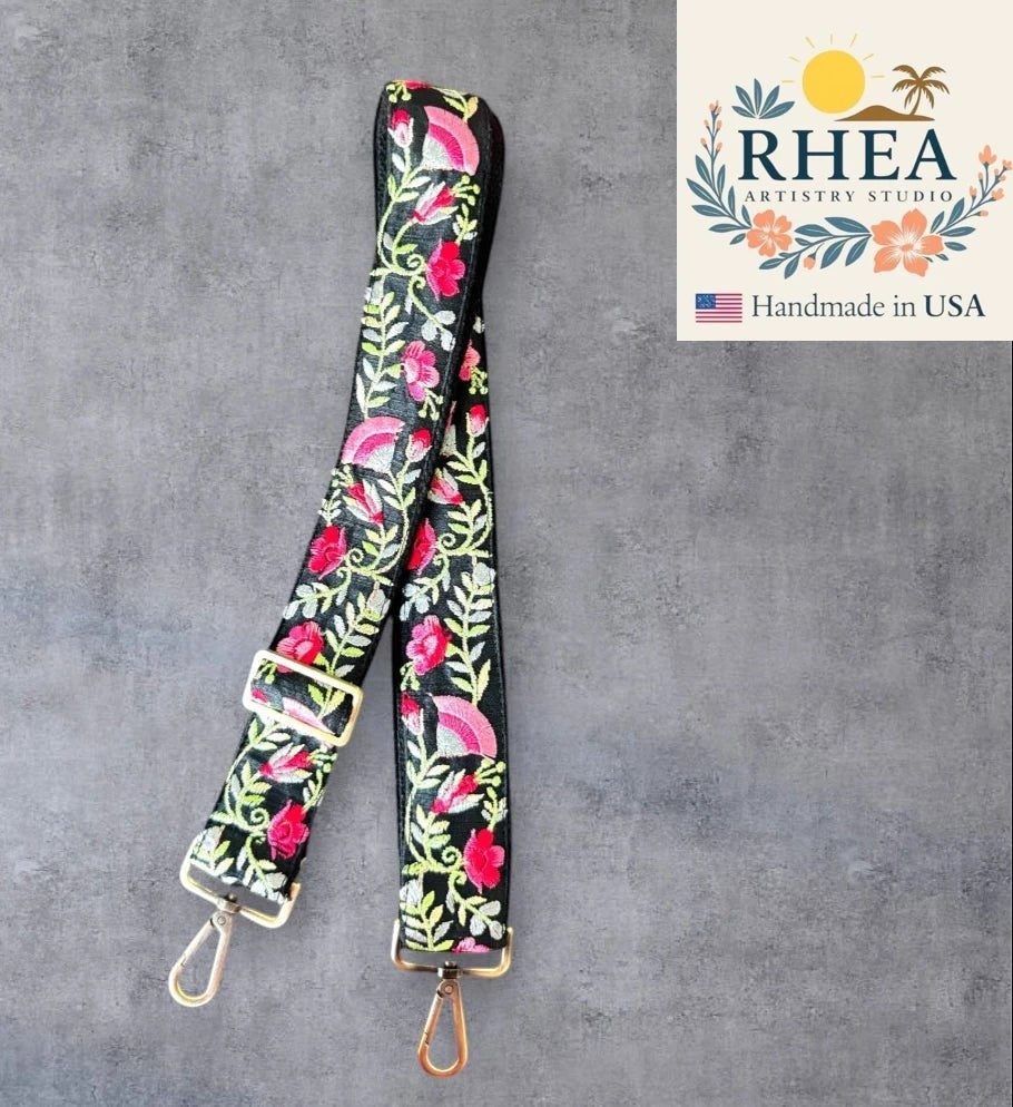 Rhea Artistry Studio black crossbody strap with embroidered pink roses and green leaves, 1.5-inch width, adjustable length, brushed brass hardware.