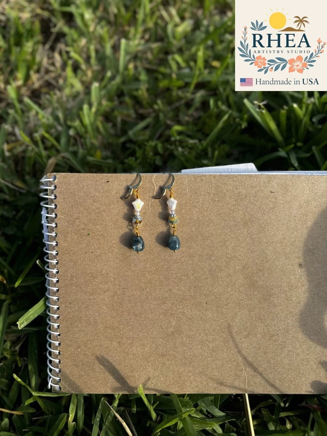 Rhea Artistry Studio white and silver floral glass drop earrings with blue gemstone and 24k gold-plated brass lever-back closures.