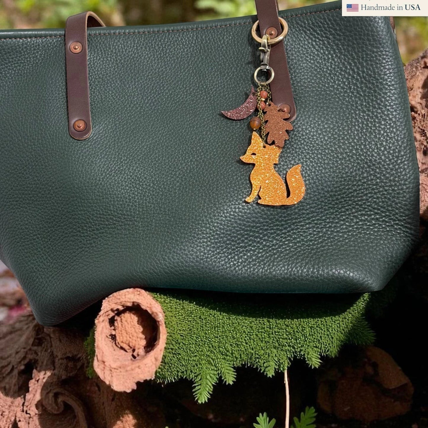 Rhea Artistry Studio glitter leather fox charm with moon and leaf accents on a dark green pebbled leather tote bag.