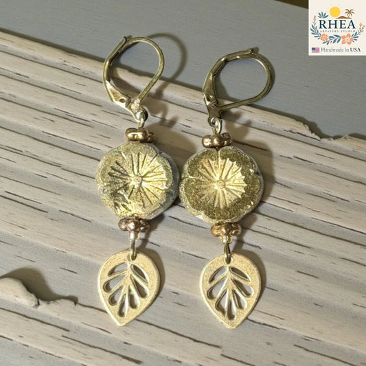 Rhea Artistry Studio handmade gold hibiscus glass drop earrings with leaf charms and lever back hooks.