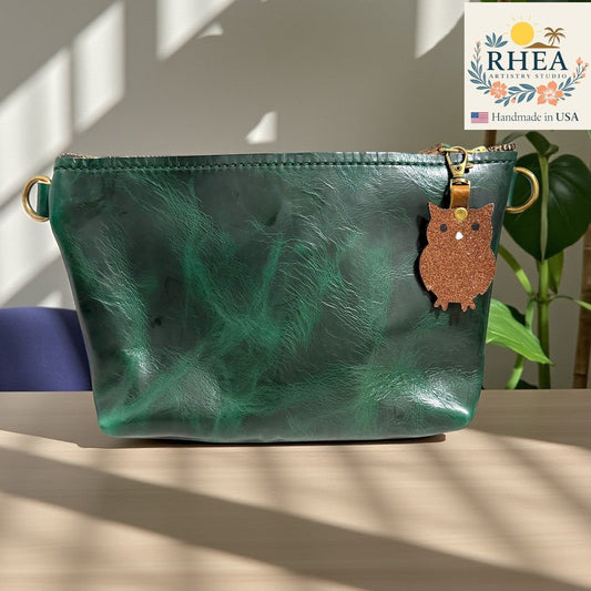 Rhea Artistry Studio dark green leather pouch with a glittery brown owl charm attached to the zipper pull.