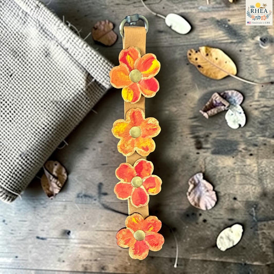 Rhea Artistry Studio Hand-Painted Leather Flower Bag Charm in Marigold Glow with orange and coral painted leather flowers, brass rivets, and antique brass clasp.